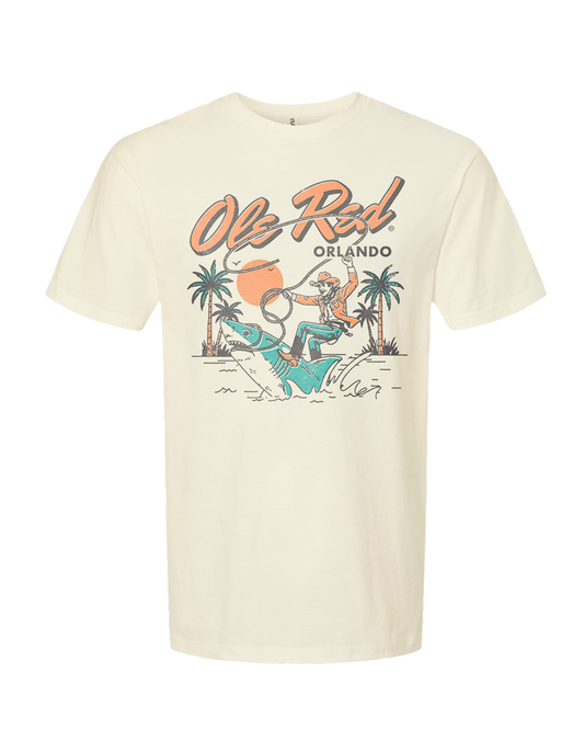Beige t-shirt with a graphic design of a person riding a dinosaur, palm trees, and 'Ole Red Orlando' text on a white background.