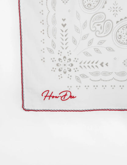 Opry paisley traveler bandana in cream with white fabric, gray paisley and floral embroidery, red edge stitching, and how den logo
